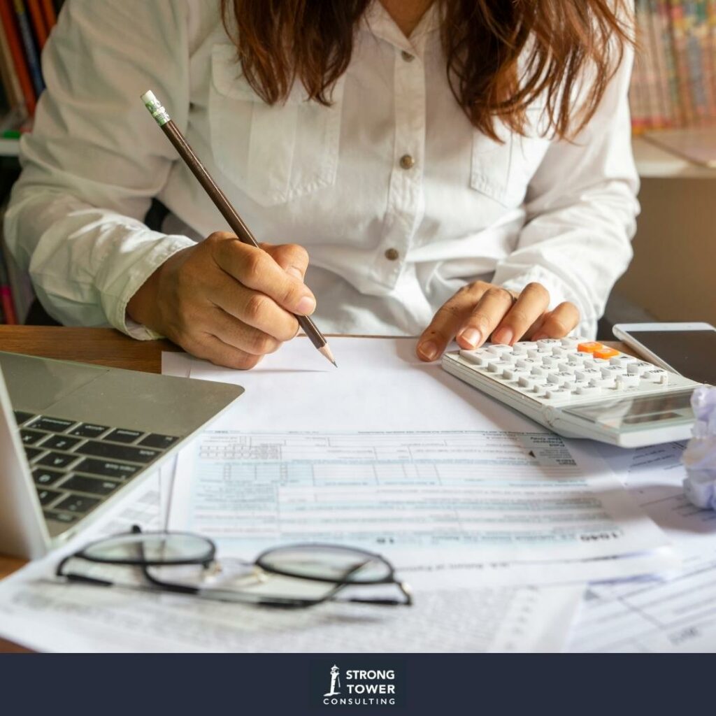 A woman doing a pen-and-paper budget with a calculator and spreadsheet.